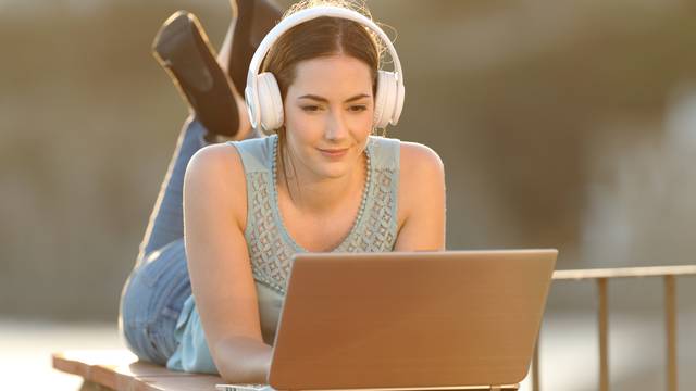 Studentin mit Kopfhörern arbeitet am Laptop im Freien